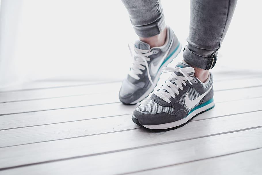 A person wearing grey and turquoise Nike trainers stands on a grey wooden floor