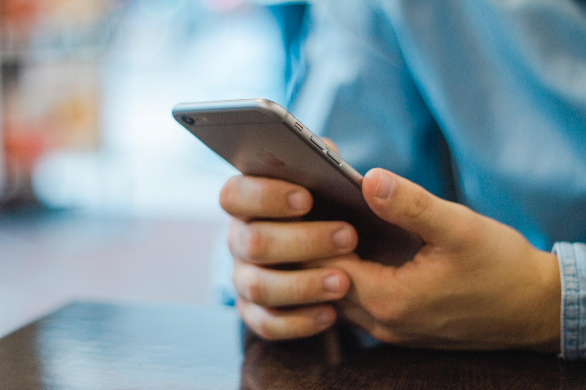 A man holding a phone as he rests his hands on a table and shops on mobile rather than desktop.