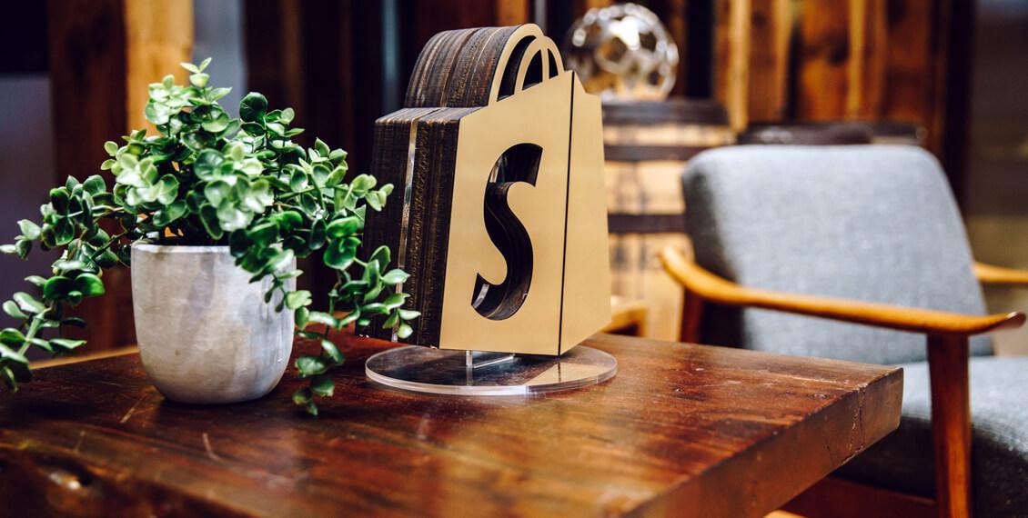 A decorative ornament in the shape of the Shopify logo rests on a stylish desk.